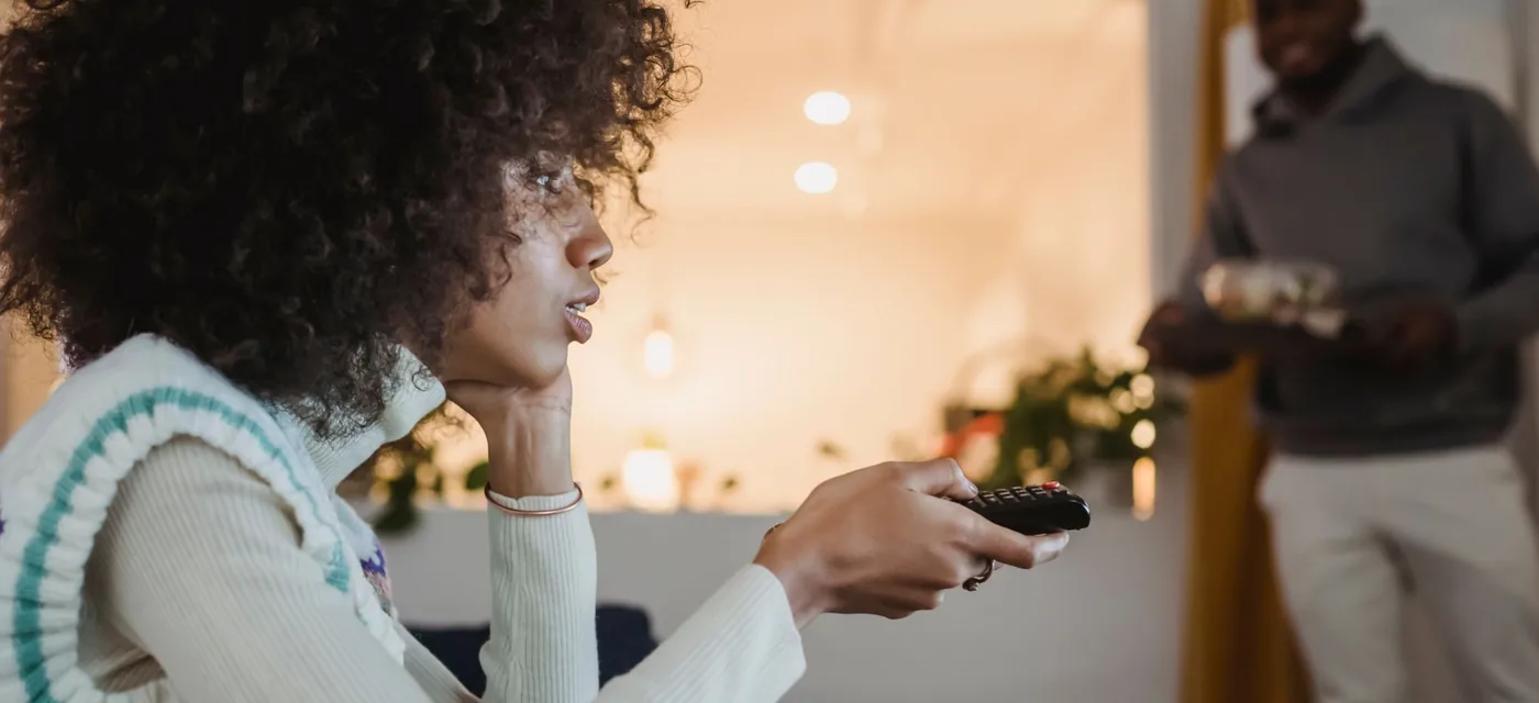 Mulher trocando de canal com o controle durante o teste IPTV grátis